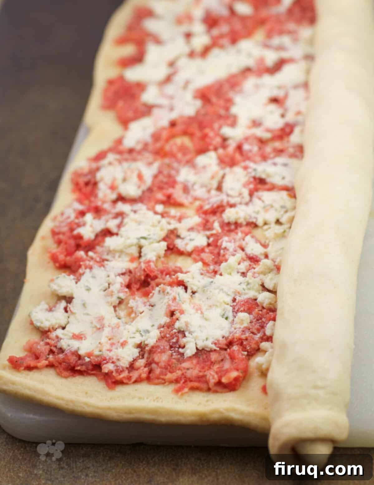Creamy Boursin Sausage Swirls 5 Hands rolling crescent dough tightly over the layers of sausage and Boursin cheese to form a log for pinwheels.