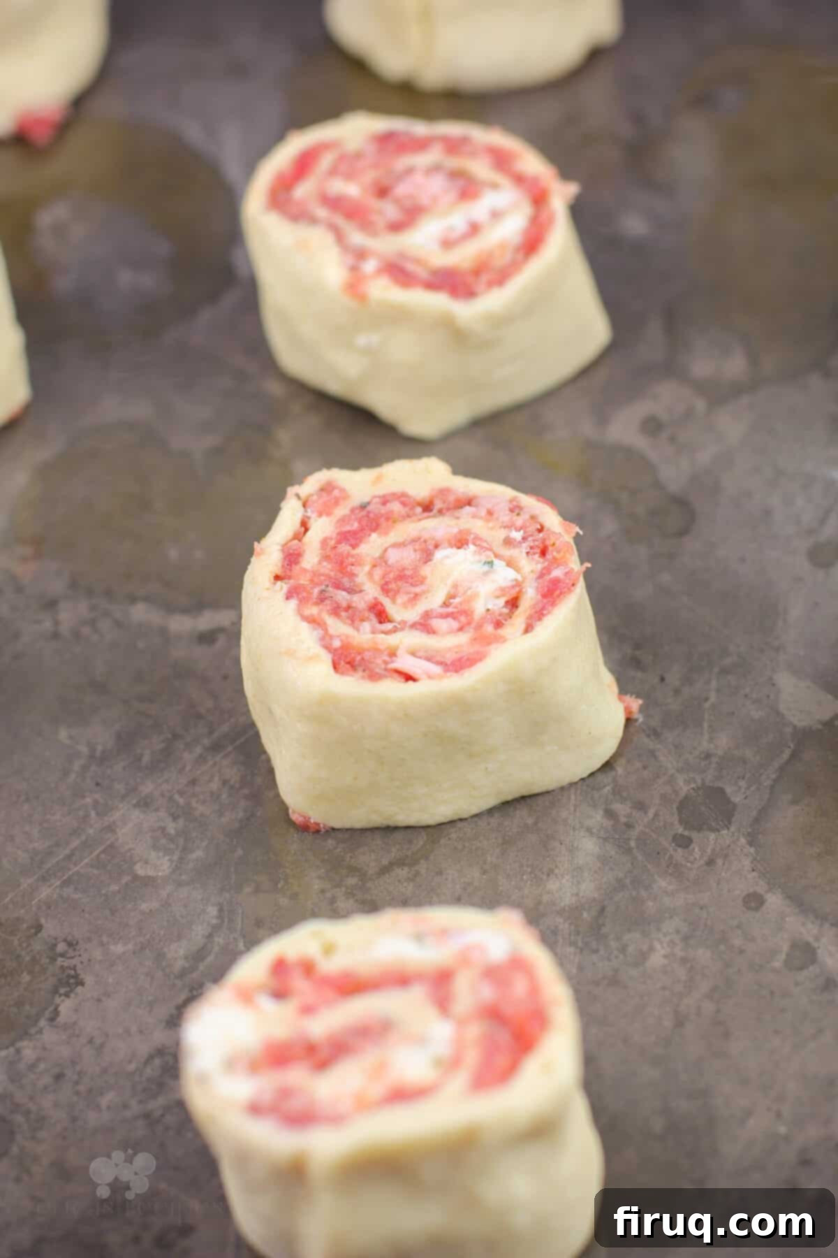 Creamy Boursin Sausage Swirls 6 Uncooked sausage and Boursin pinwheels neatly arranged on a baking sheet, ready for the oven.