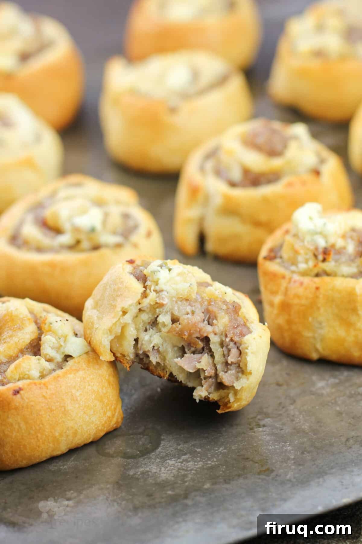 Creamy Boursin Sausage Swirls 8 Close-up of baked sausage pinwheels on a baking sheet, with one pinwheel showing a bite taken out, revealing the savory sausage and creamy Boursin layers.