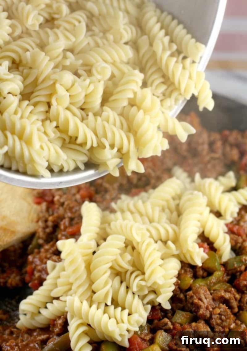 Homestyle Beef & Macaroni Bake 7 cooked pasta being poured into a skillet with the rest of the sloppy joe ingredients, ready to be mixed