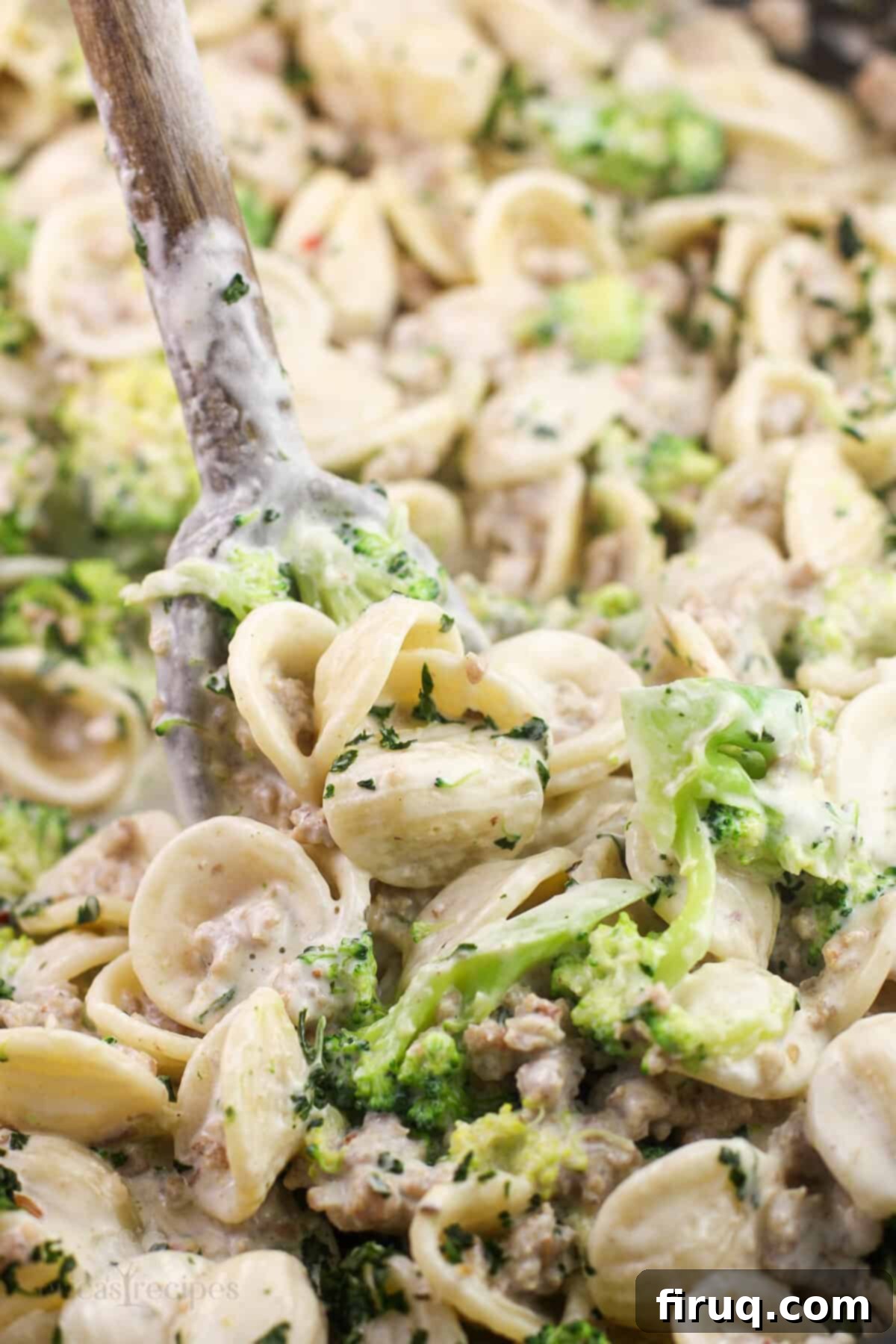 Sausage and Broccoli Orecchiette 2 A wooden spoon rests in a large pan filled with creamy broccoli and sausage orecchiette pasta, ready to serve.