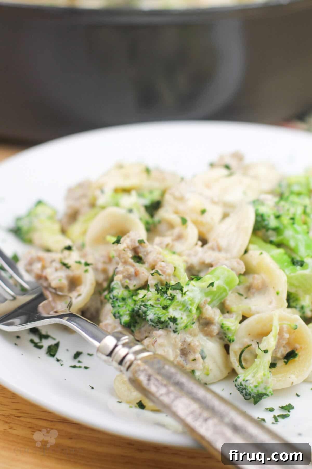 Sausage and Broccoli Orecchiette 5 A portion of creamy broccoli and sausage orecchiette pasta on a white plate with a fork, ready to be eaten.