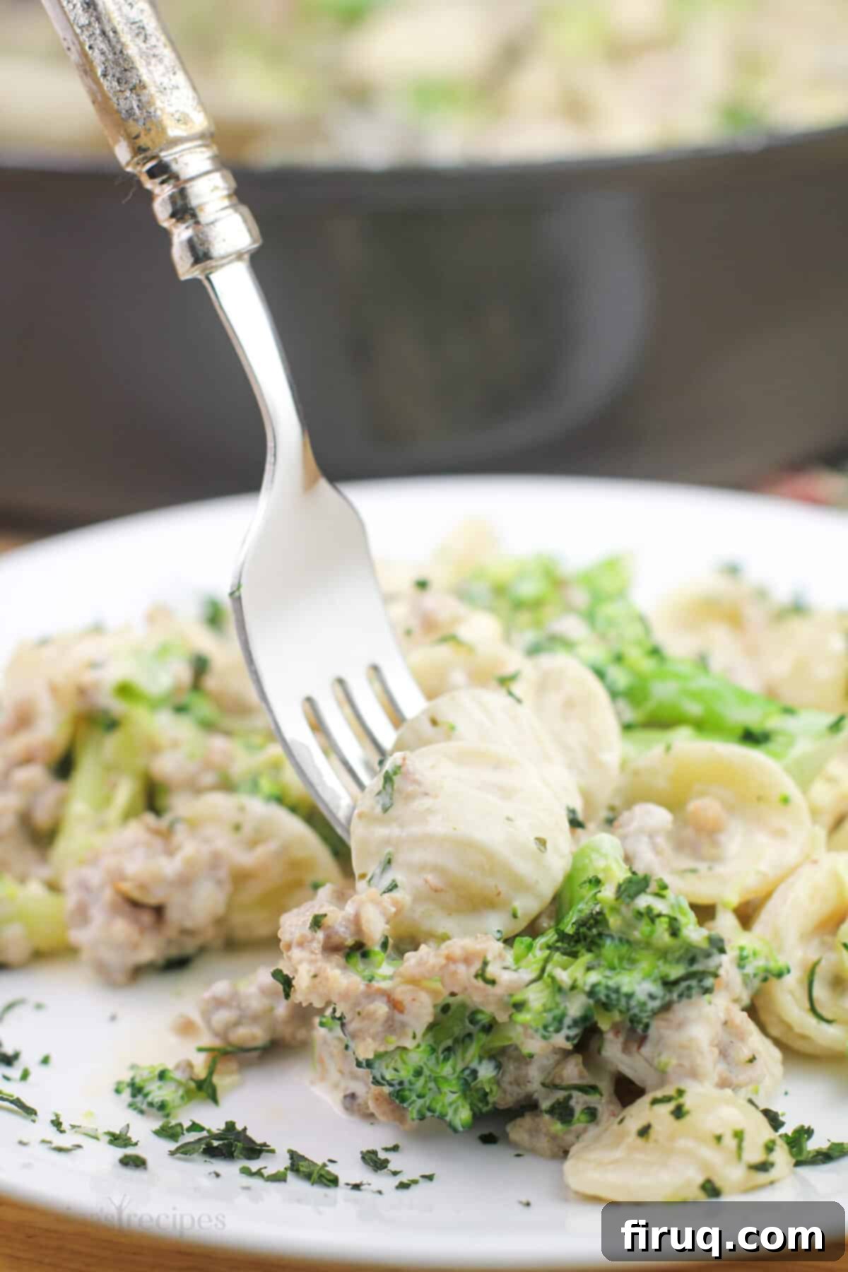 Sausage and Broccoli Orecchiette 6 A fork lifts a generous portion of creamy broccoli and sausage orecchiette pasta from a white dish.