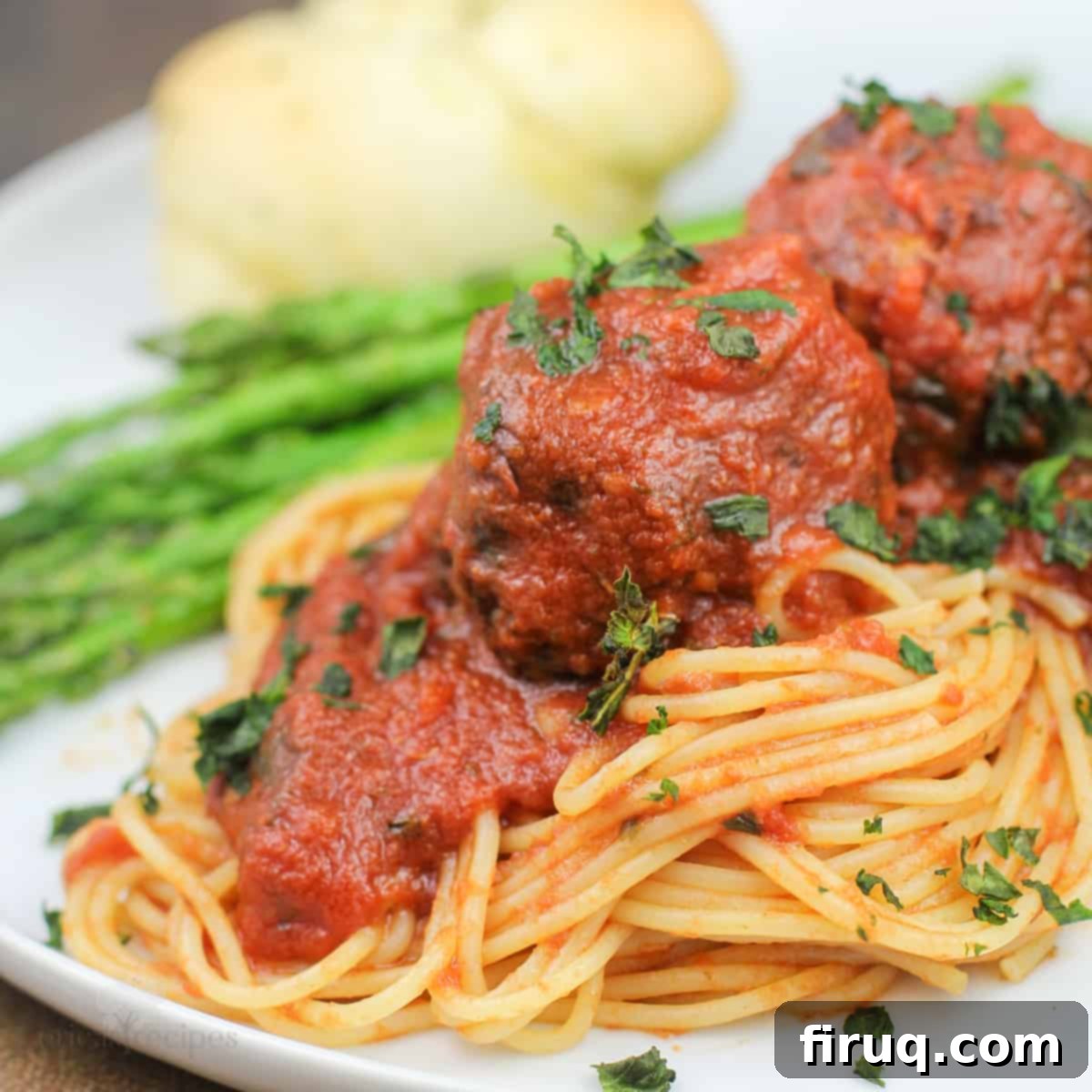 Smoky Meatballs in Tangy Marinara 2 plated portion of smoked meatballs marinara on sauce on spaghetti (asparagus and roll in background)
