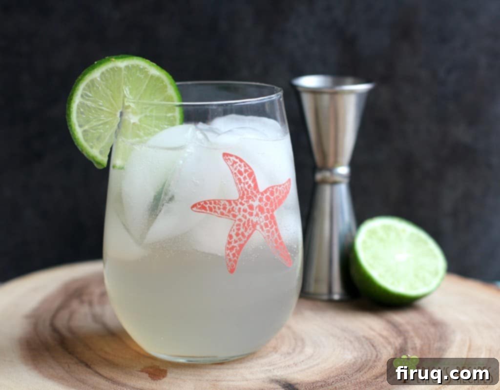 Ruby Renewed 2 A tall glass filled with ice and a pink grapefruit vodka cocktail, garnished with a fresh lime wedge. A decorative pink starfish decal is on the side of the glass.