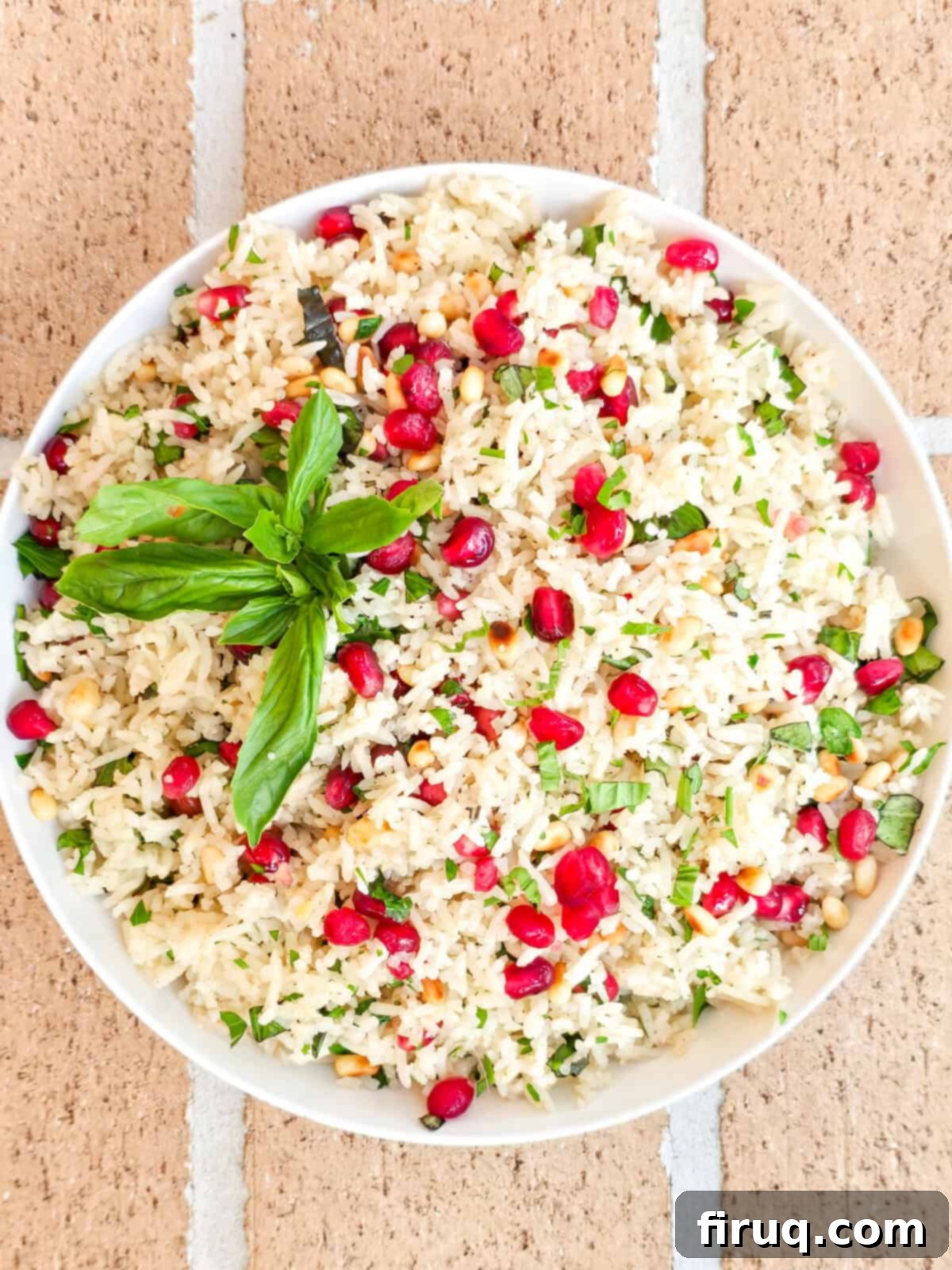 Fresh pomegranate vegan rice pilaf garnished with basil leaves, served in a white bowl on a rustic background