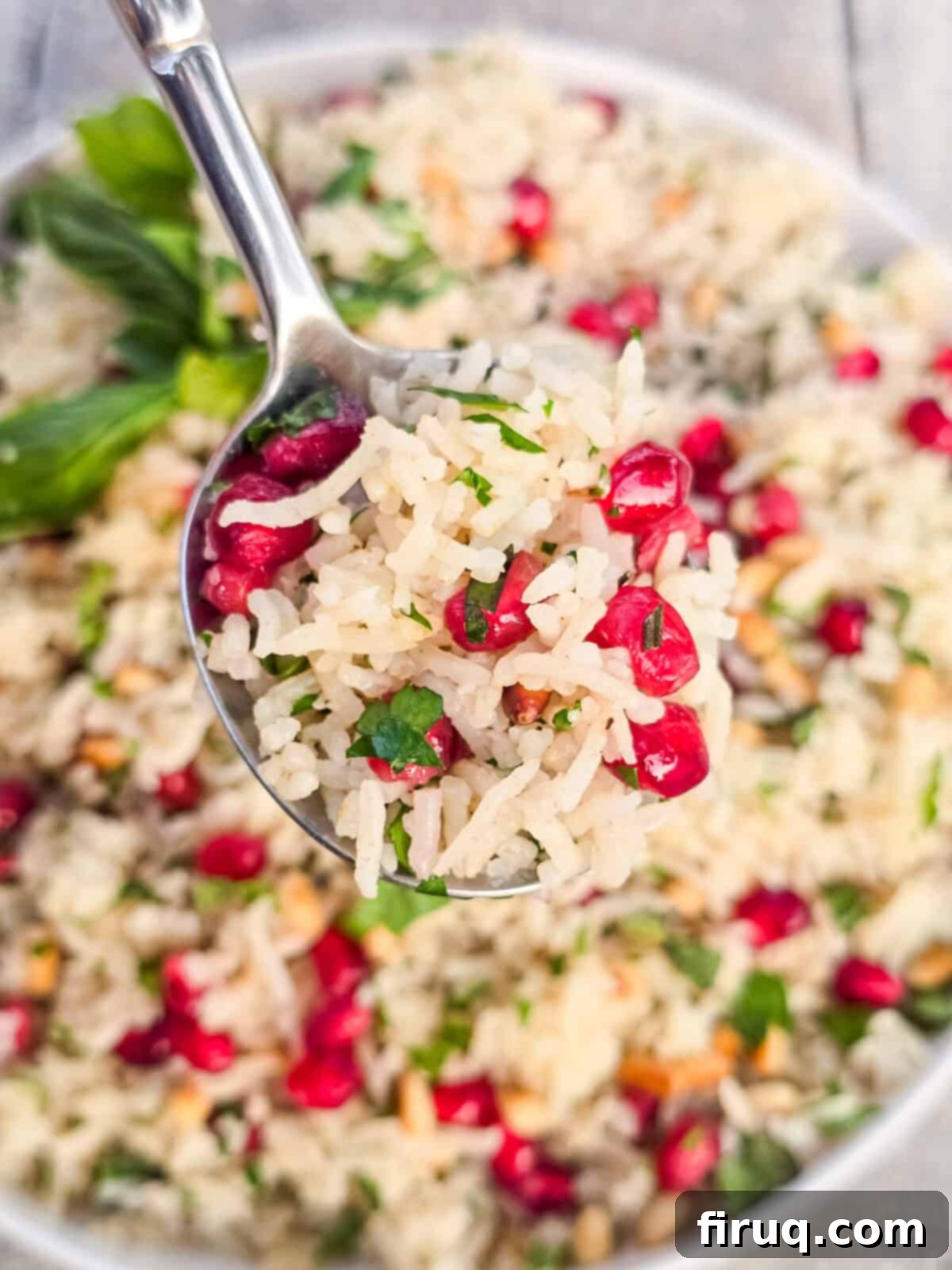 Pomegranate vegan rice pilaf with herbs and pine nuts in a white bowl, close-up.