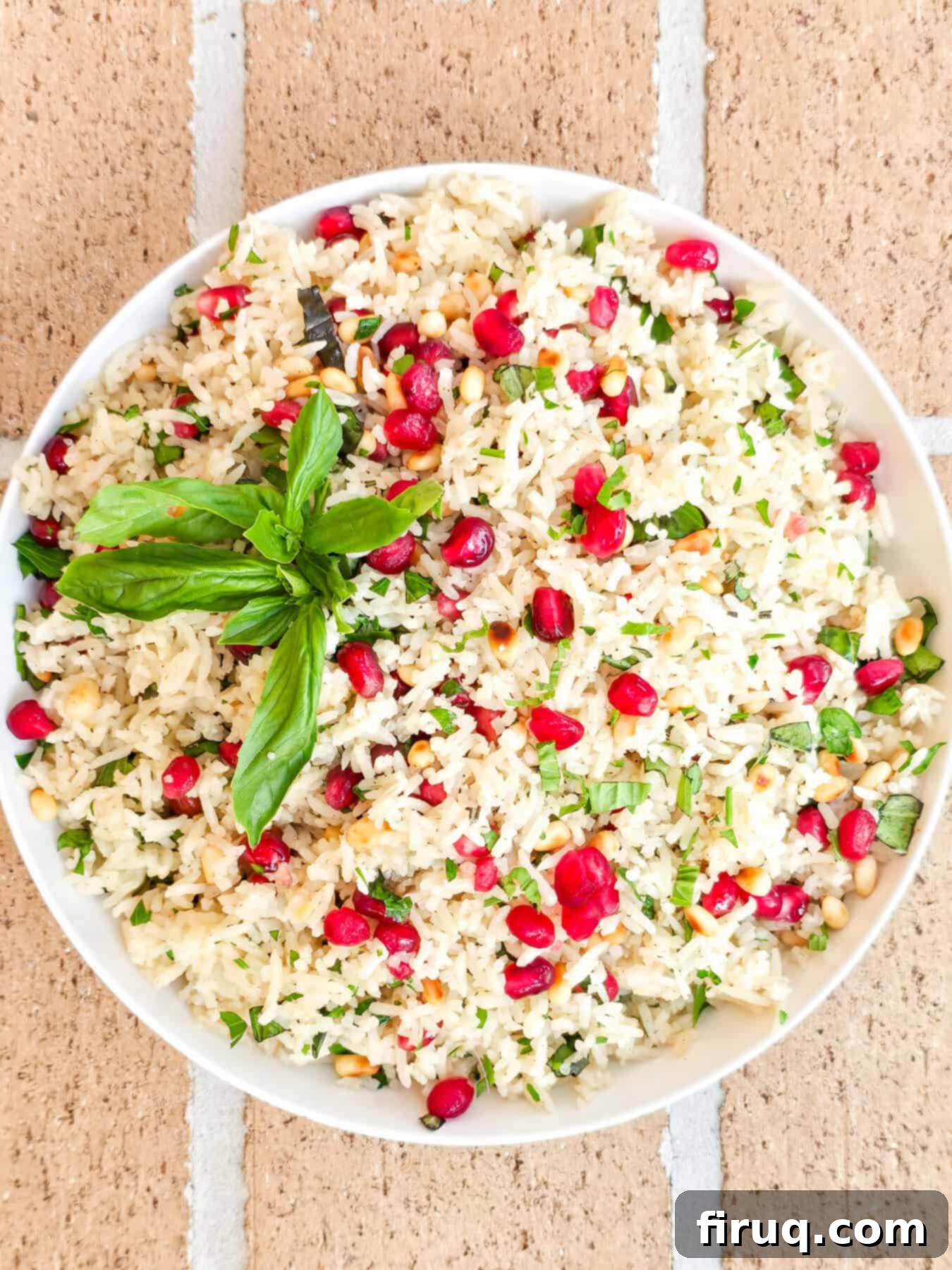 Fresh pomegranate vegan rice pilaf garnished with basil leaves, served in a white bowl on a rustic background